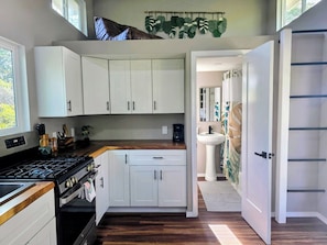 A modern kitchen with white cabinets, a stove, and a sink. - Koa + Paka: Embrace the elements in style (Keaau)