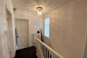 A narrow hallway with a white door, a radiator, and a window with blinds. - Room-double Spacious Room Near CBS Arena (Coventry)