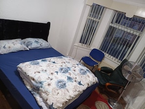 A bedroom with a bed, two chairs, a fan, and a window with blinds. - Room-double Spacious Room Near CBS Arena (Coventry)