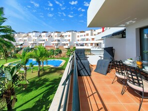 Un balcó amb mobles de jardí, una piscina i vista a una zona residencial amb edificis blancs.
