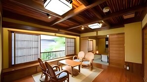 Ein traditioneller japanischer Raum mit Tatami-Böden, einem niedrigen Tisch mit Stühlen und großen Fenstern mit Blick auf Grünflächen.