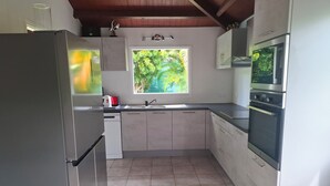 Cozinha equipada com geladeira, forno, micro-ondas e janela com vista para o verde.