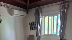 Quarto com cama, cadeira, janela com cortinas e ar condicionado fixado na parede.