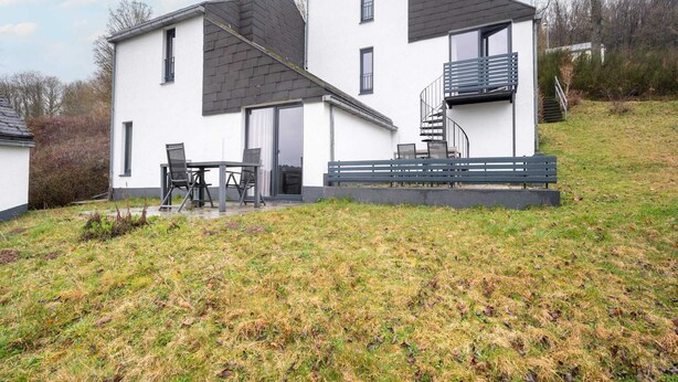 Een modern huis met twee verdiepingen, een balkon, een terras met tuinmeubilair en een gazon.