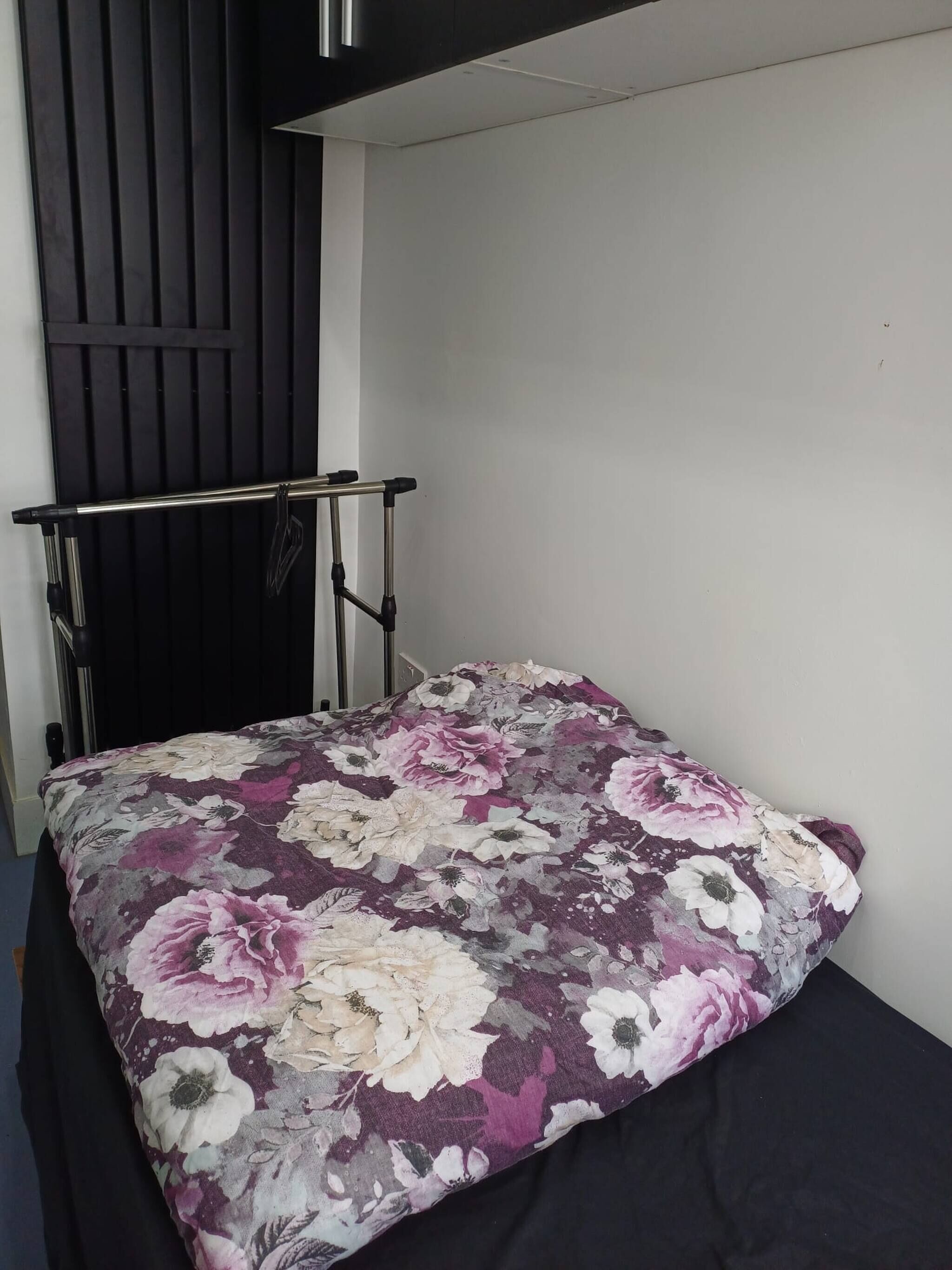 A small bed with a floral bedspread in a room with a dark vertical panel and a metal railing.