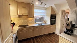 A kitchen with wooden cabinets, a washing machine, a coffee machine, and a window with a view. - Room-single Cosy Room Near CBS Arena and (Coventry)