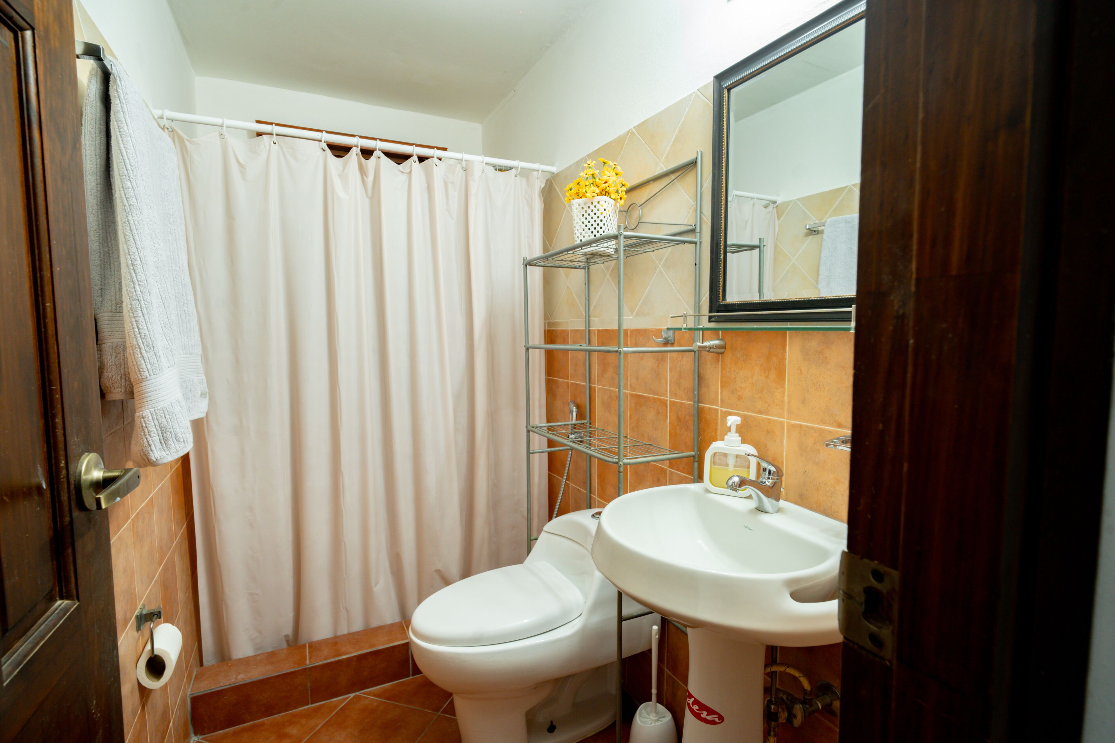 A bathroom with a toilet, sink, shower curtain, and a mirror.