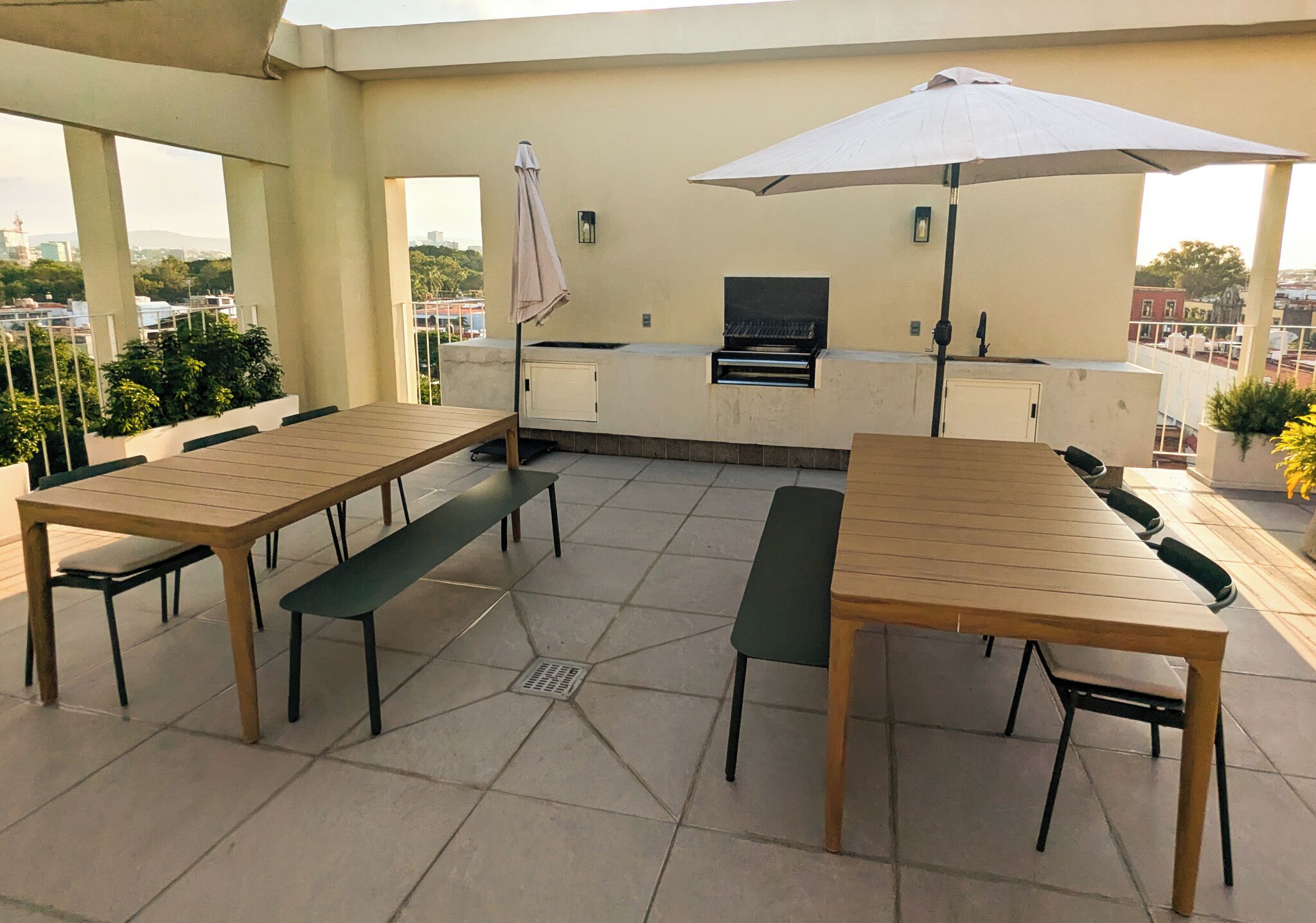 An outdoor patio with a wooden table and benches, a grill, and a large umbrella.