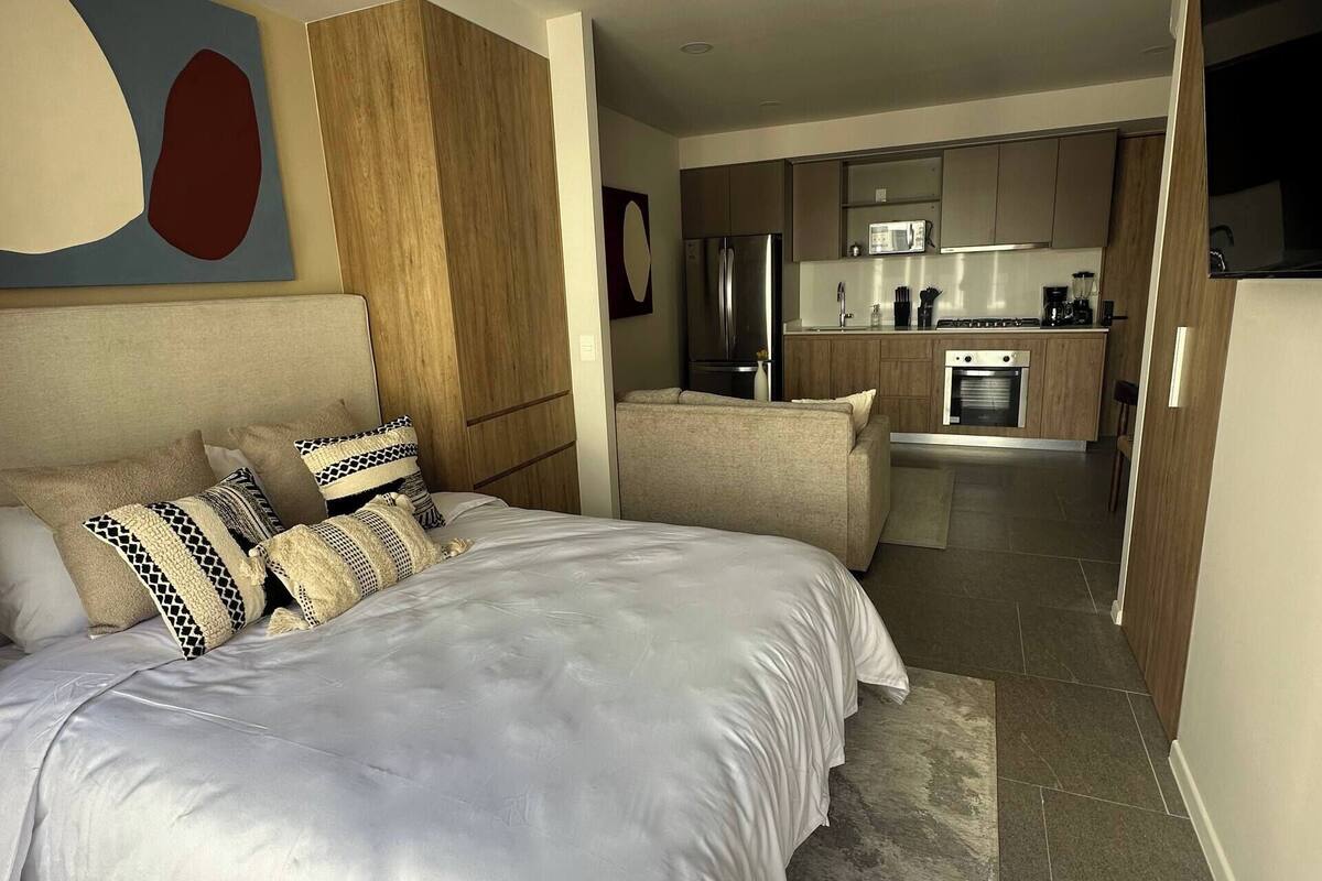 Une chambre moderne avec un grand lit, un coin cuisine à l’arrière-plan et un espace repas.