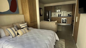 Un dormitorio moderno con una cama grande, una kitchenette al fondo y un comedor.
