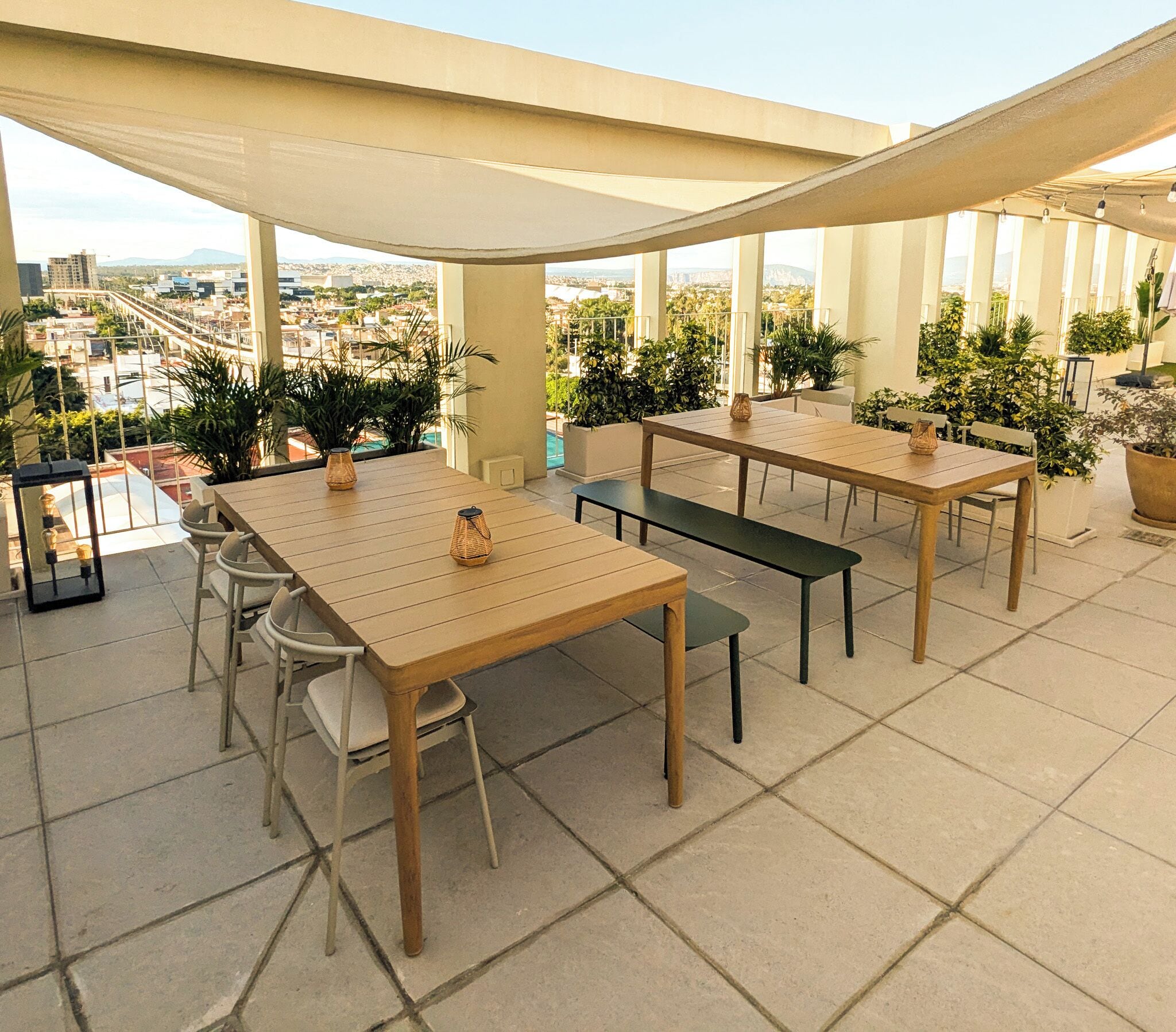 An outdoor patio with tables and chairs, potted plants, and a view of the cityscape.