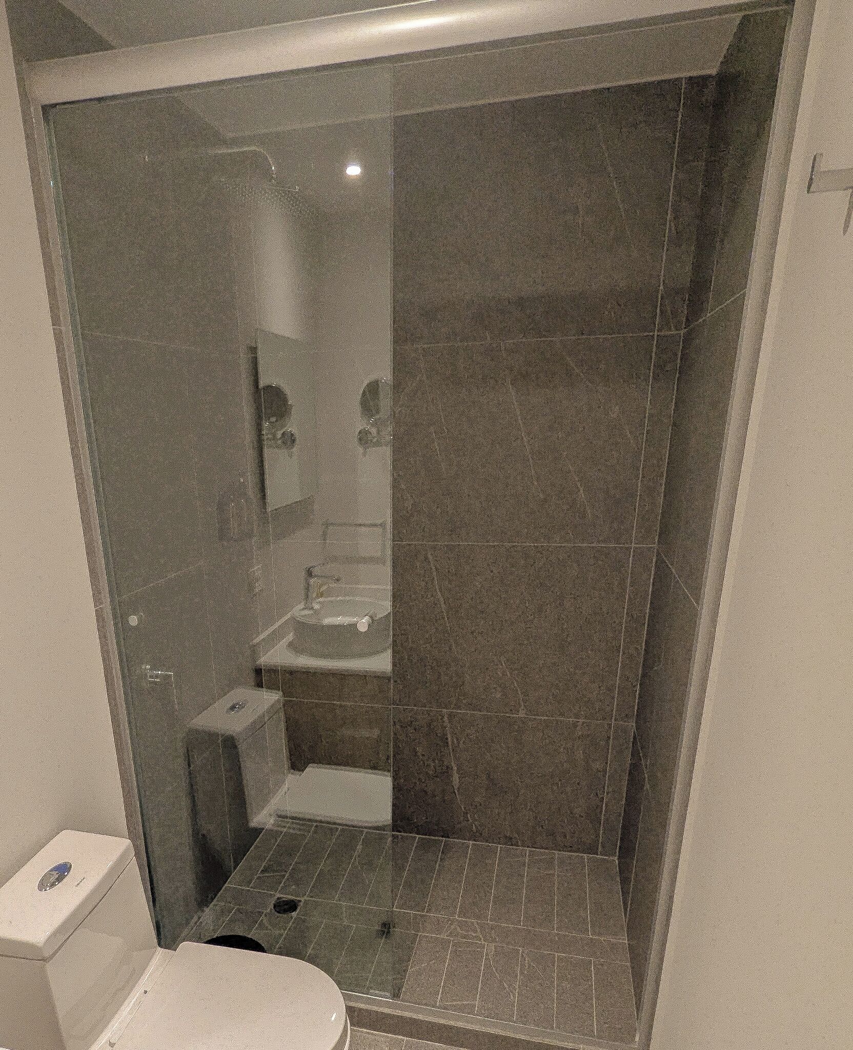 A small, enclosed bathroom with a glass door, a toilet, a sink, and a shower area.