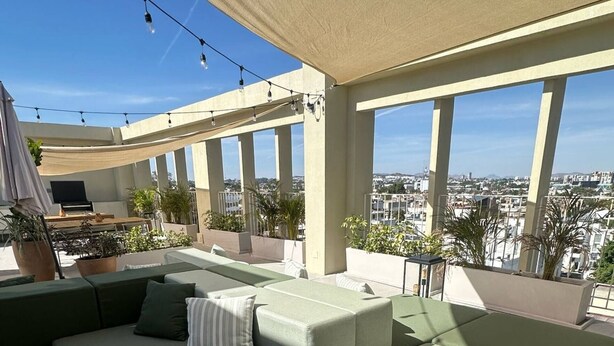 Terraza en la azotea con sofá modular, plantas en macetas y vista panorámica de la ciudad.