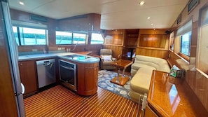 A compact kitchen with a dishwasher, oven, and a small island with a sink. There is a seating area with a cushioned sofa and a small table.