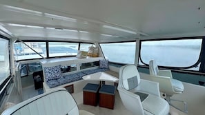 A boat interior with a dining area, seating, and a view of the water.