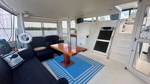 A boat interior with a dining area, seating, and a view of the water. - Reel Excuse - Yacht Living (Fort Myers Beach)