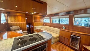 A compact kitchen with a stove, a dining area with a table and chairs, and a seating area with a cushioned bench. - Reel Excuse - Yacht Living (Fort Myers Beach)