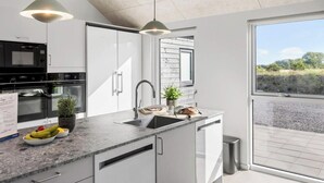 A modern kitchen with white cabinetry, a built-in oven, a sink, and a window overlooking a landscape. - 5 Star Holiday Home in Idestrup (Idestrup)