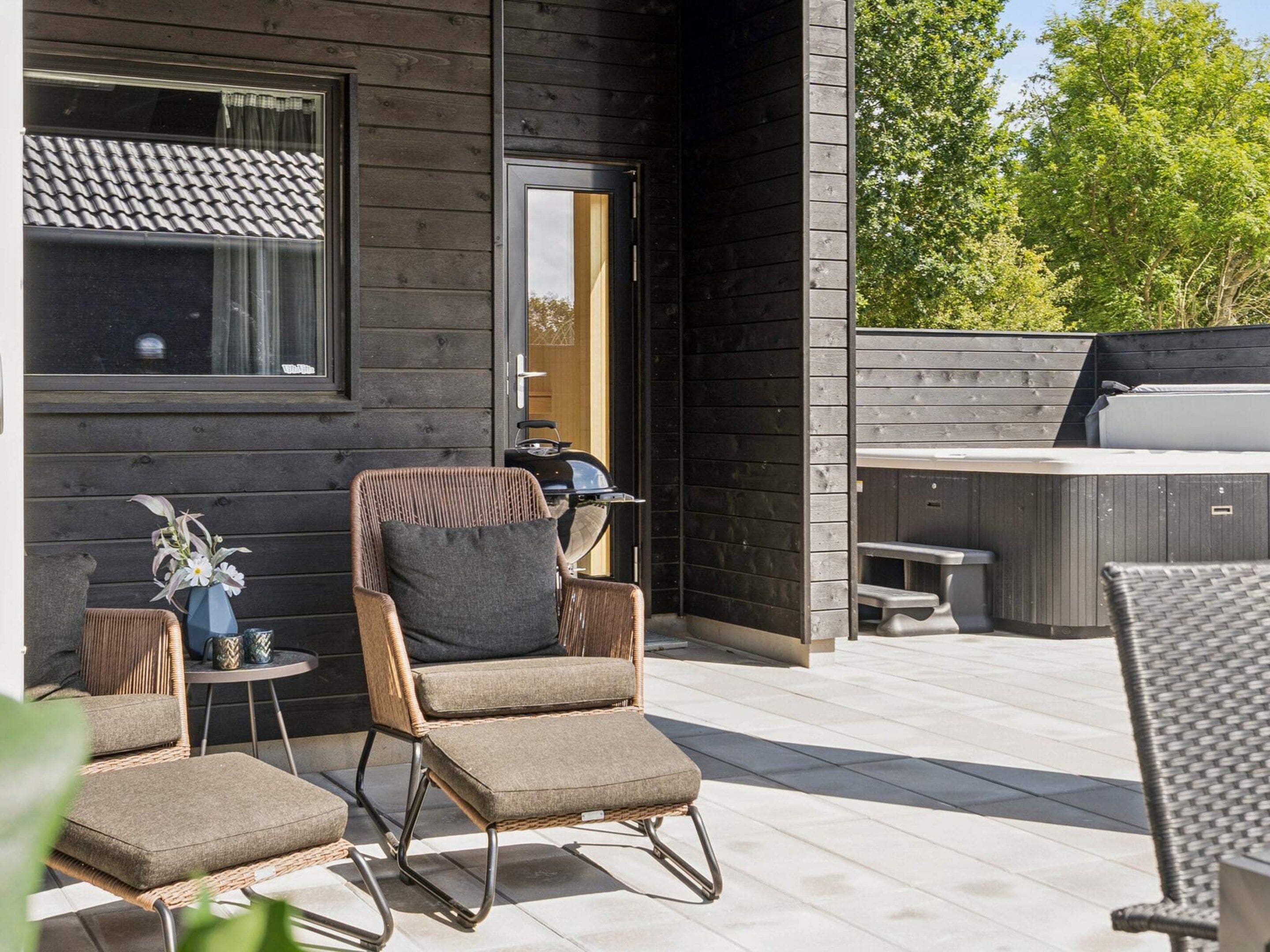 Un espace extérieur moderne, aménagé avec des chaises en osier et une petite table, un barbecue et une terrasse en bois.