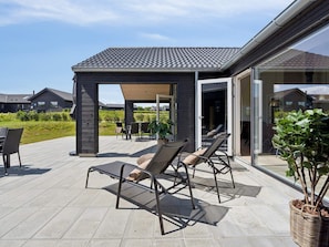 An outdoor patio with two lounge chairs and a table, a covered seating area, and a view of a residential neighborhood. - 5 Star Holiday Home in Idestrup (Idestrup)