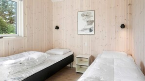 A room with two beds, a small white nightstand, a framed picture on the wall, and a window. - 5 Star Holiday Home in Idestrup (Idestrup)