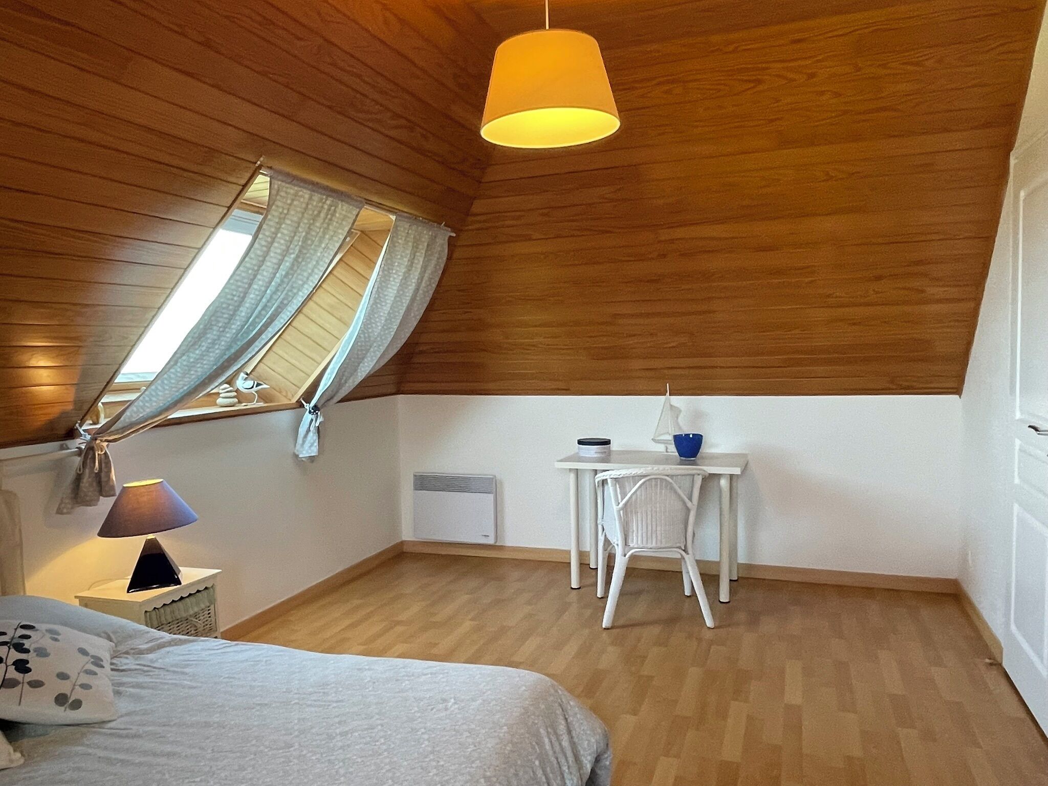 Une chambre à coucher avec un lit, un bureau, une chaise, une lampe et une fenêtre avec des rideaux.