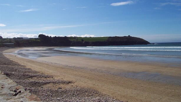 Une plage au rivage de galets, avec une côte sinueuse et une colline qui se dessine à l’horizon.