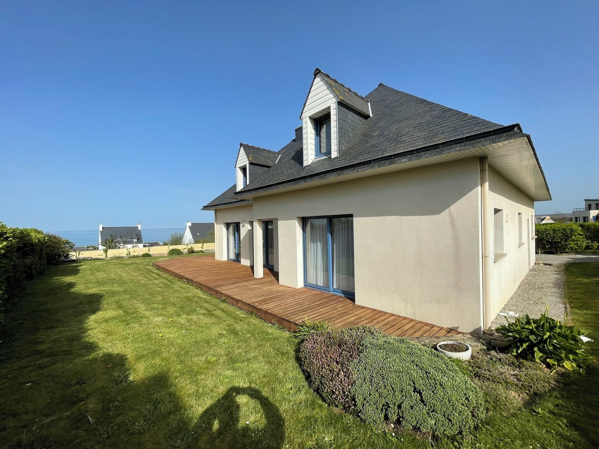 A modern house with a wooden deck, large windows, and a view of the sea.