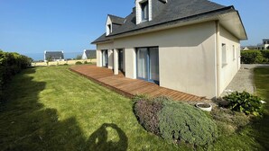 Une maison moderne dotée d’une terrasse en bois, de grandes fenêtres et offrant une vue sur la mer.