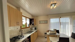 Une cuisine dotée de meubles en bois, d’une cuisinière à gaz, d’un four à micro-ondes et d’un coin repas avec une table et des chaises.