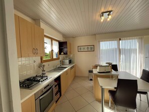 A kitchen with wooden cabinets, a gas stove, a microwave, and a dining area with a table and chairs. - D6054-Holiday home in Plomodiern with quiet garden and sea view! (Plomodiern)