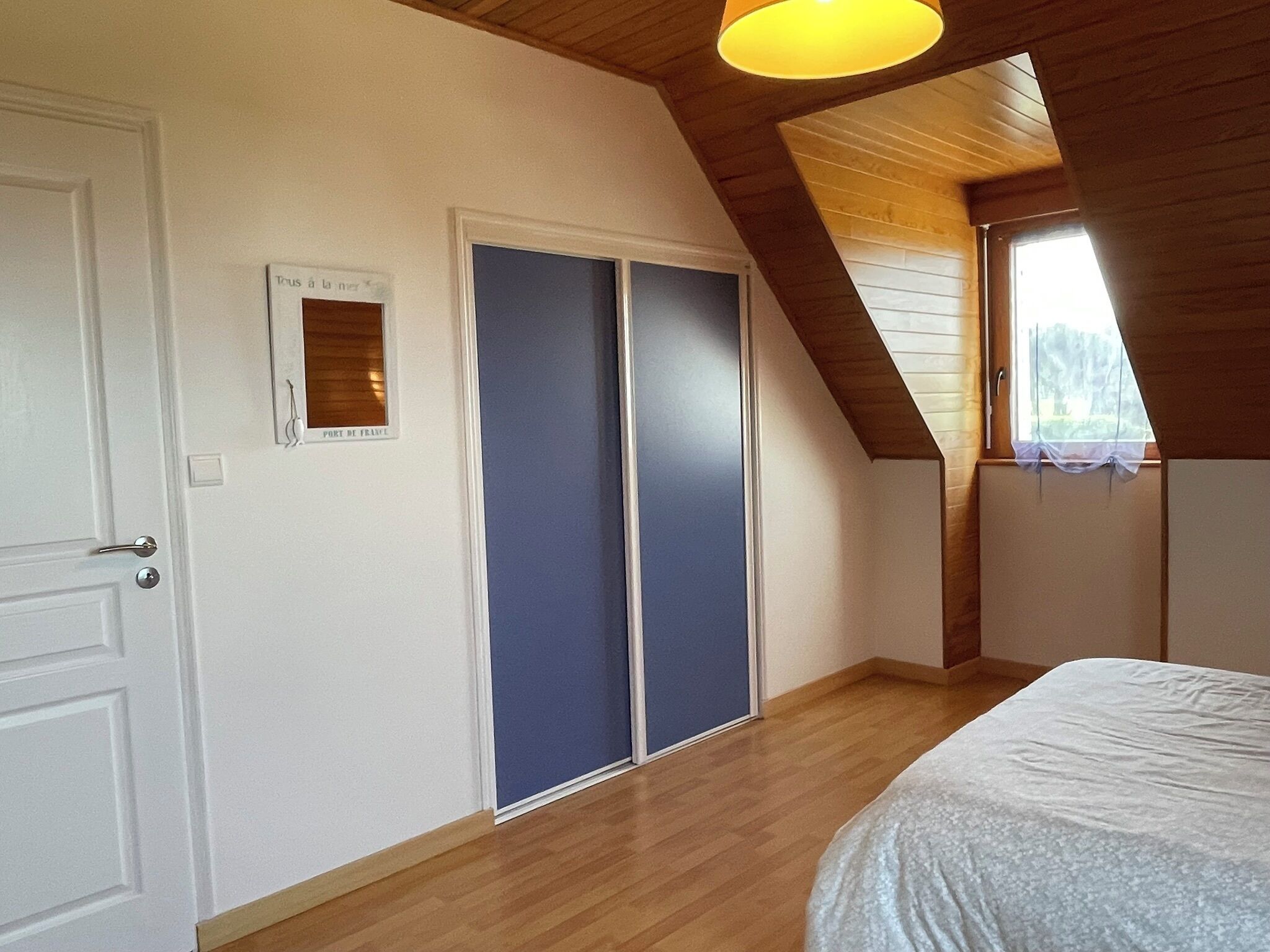 A bedroom with a sloped ceiling, a bed, a wardrobe, and a window.