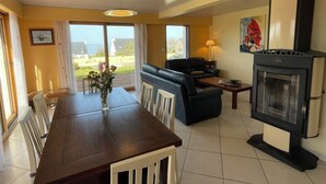 Un espace repas comprenant une table et des chaises en bois, un canapé, une cheminée et une vue sur l’extérieur.