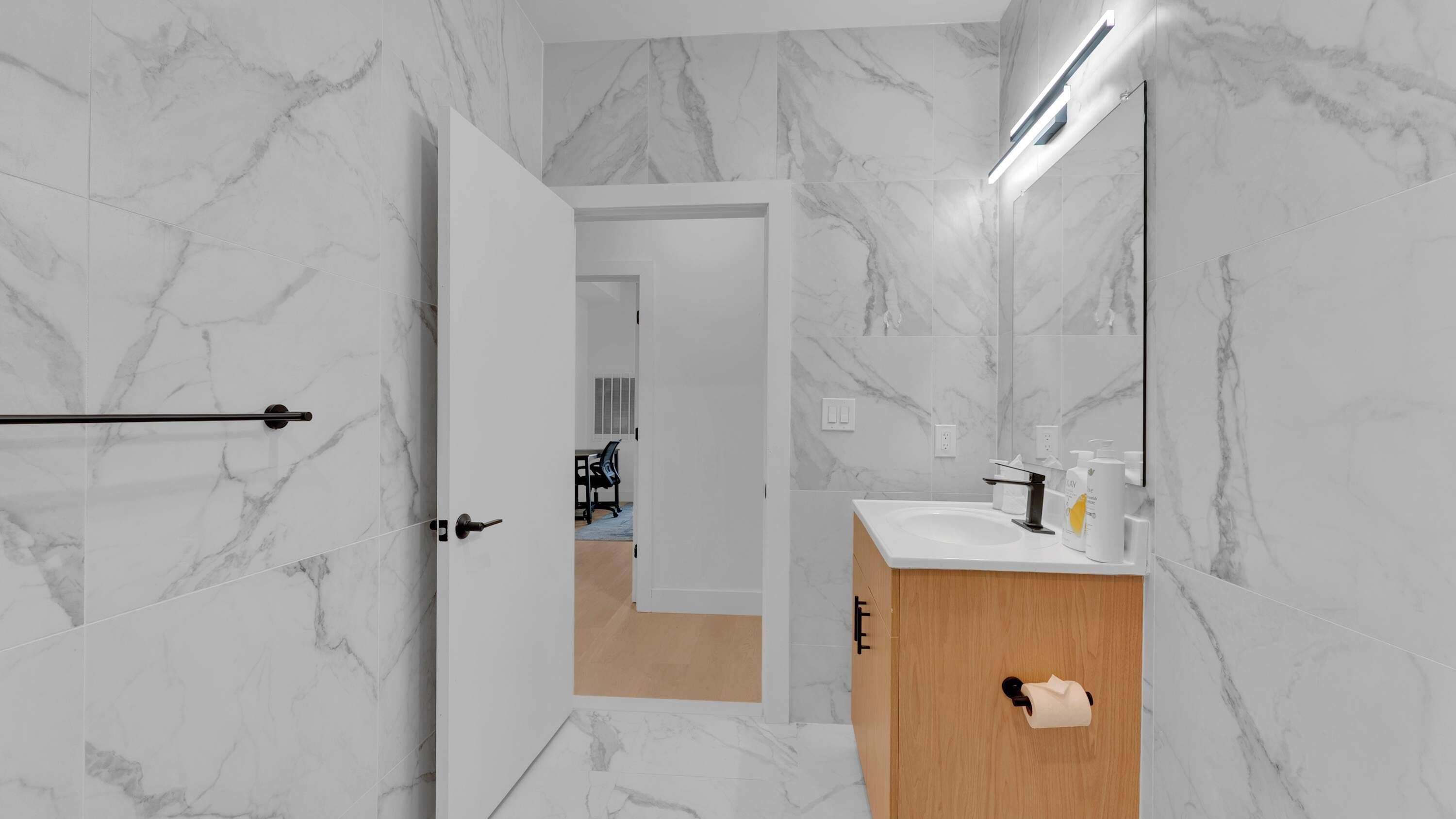 A bathroom with marble walls, a wooden cabinet, a mirror, and a towel dispenser.