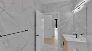 A modern bathroom with marble walls, a white sink, and a door leading to another room. - Trendy NoLibs 1BR Near City Spots | Sleeps 4 (Philadelphia)