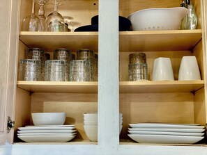 Ein Holzschrank mit Regalen, gefüllt mit Glasbehältern, weißen Schüsseln und Tellern.