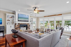 A living room with a fireplace, a television, and a ceiling fan. - Waterfront Retreat w/ Private Pool, Dock, Theater Room & Boat Access (Cape Carteret)