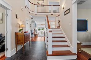 A multi-level home interior with a staircase, wooden flooring, and a hallway leading to a living area. - Waterfront Retreat w/ Private Pool, Dock, Theater Room & Boat Access (Cape Carteret)