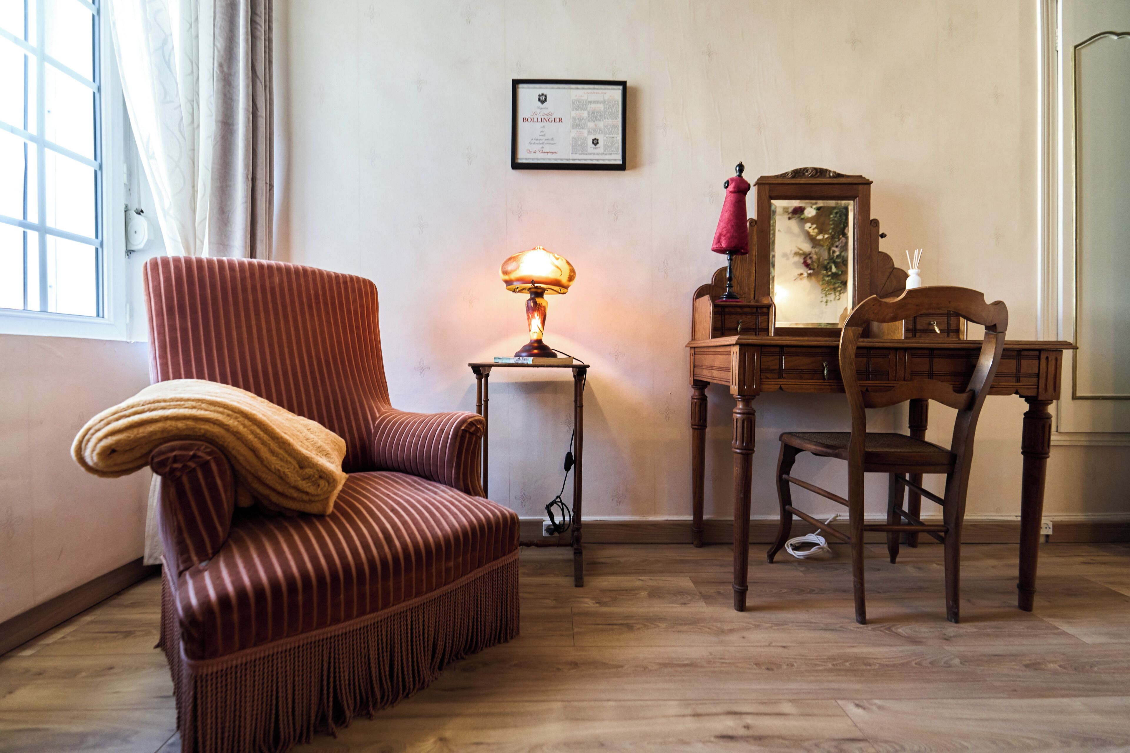 Une pièce avec un fauteuil à rayures, un bureau avec un miroir et une lampe.