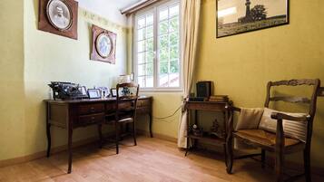 Una habitación con un escritorio de madera, una silla, una ventana con cortinas y cuadros en la pared.