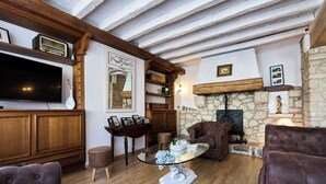 A living room with a stone fireplace, wooden beams, a flat-screen TV, and leather sofas.