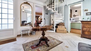 A spacious living area with a round wooden table, a white bench, a large mirror, and a spiral staircase.