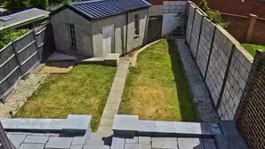 Un patio en la azotea con baldosas de piedra, un cobertizo pequeño y una zona con césped.