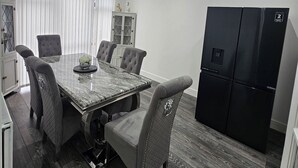 Un comedor con una mesa de mármol, sillas tapizadas grises, un refrigerador negro y un ventilador de techo.