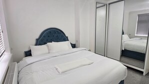 Una cama bien hecha con sábanas blancas, cabecera oscura y toalla blanca.