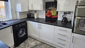 Una cocina moderna con armarios blancos, lavadora negra, extractor de acero inoxidable y salpicadero de azulejos.