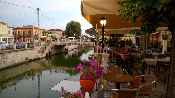 Un café situé au bord du canal, avec une terrasse, un pont de pierre et un quai pour les bateaux.