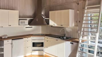 Una cocina con armarios blancos, horno empotrado, microondas, pileta de acero inoxidable y encimera de madera.