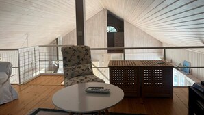 A high-ceilinged room with a wooden slatted ceiling, a round table with a remote control, a floral-patterned chair, and a wooden crate with a lattice design. - 5 Star Holiday Home in Ingaro (Ingaro)