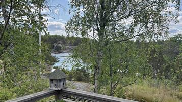 Un puente de madera con un comedero para pájaros y una planta en maceta, con vistas a un cuerpo de agua y árboles.
